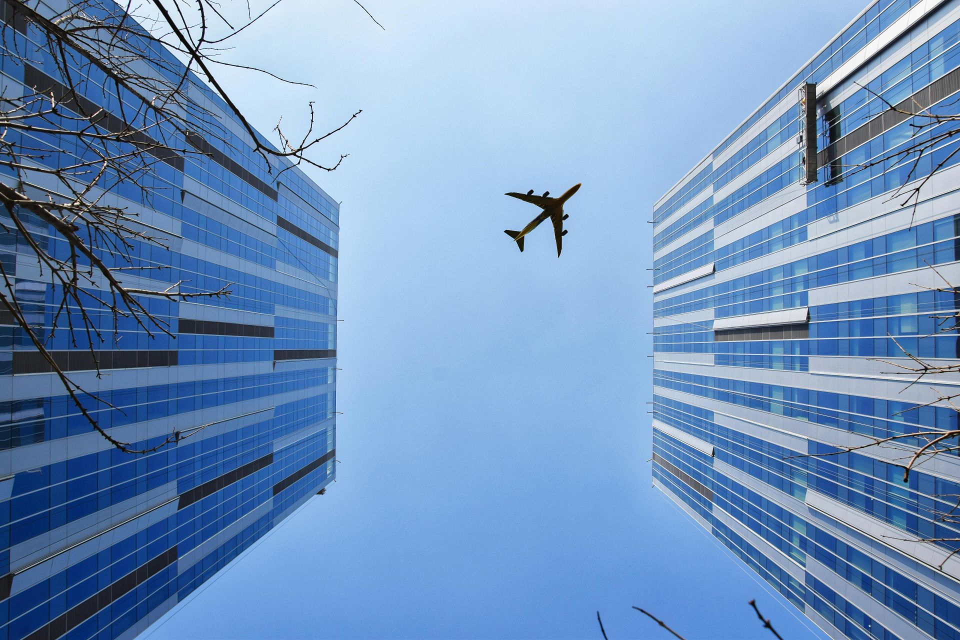 A striking low angle shot capturing skyscrapers and an airplane above a clear blue sky.