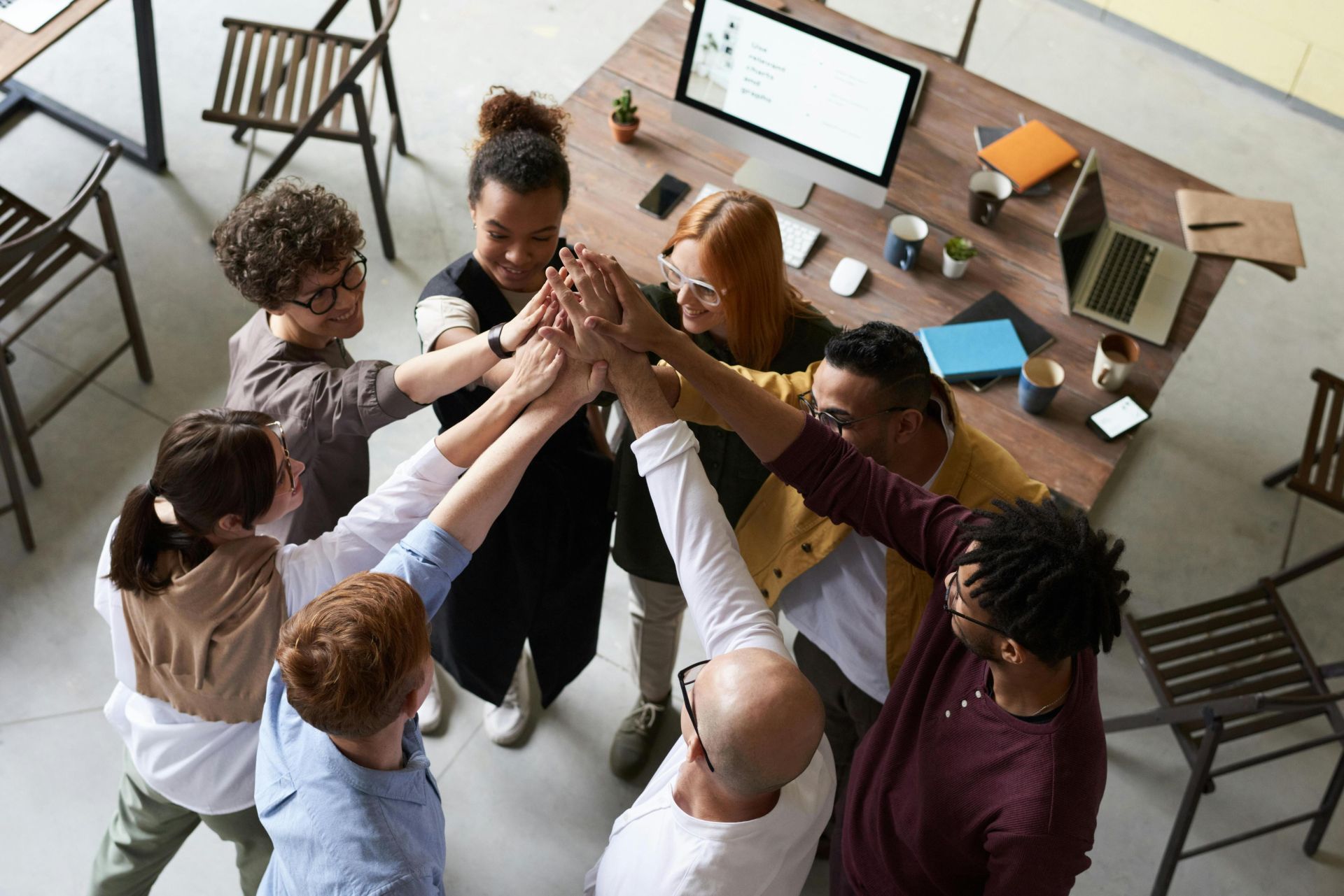 A diverse group of colleagues giving a high five during a corporate meeting indoors.